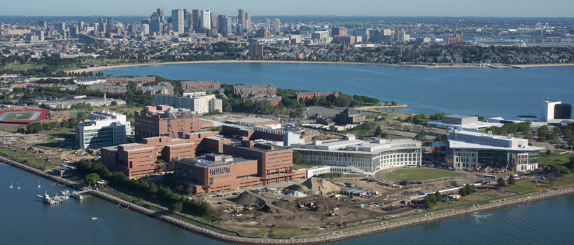 A helicopter view of UMass Boston, the water that surrounds the peninsula, and the Boston skyline behind it